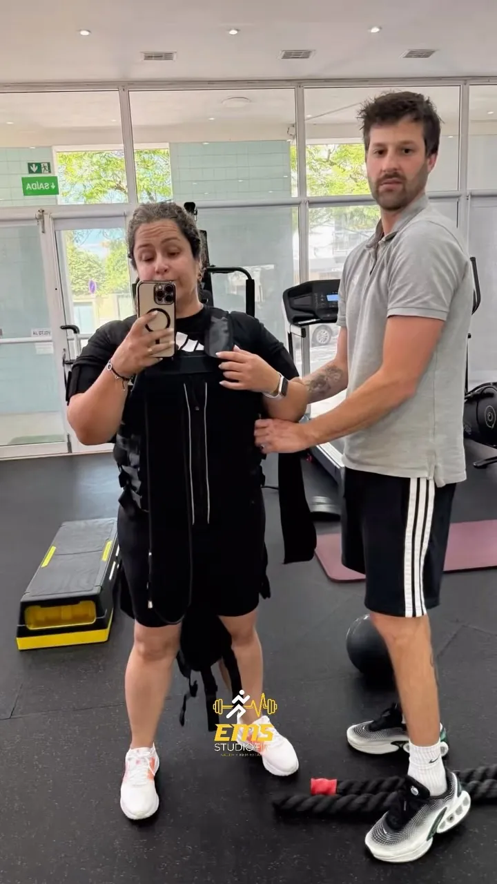 O professor ajusta o fato de eletroestimulação a uma aluna antes do treino