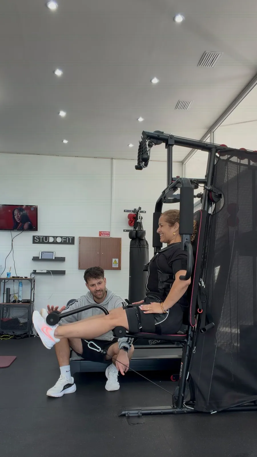 O PT Guilherme Figueiredo acompanha uma aluna com fato de eletroestimulação num exercício de pernas no estúdio